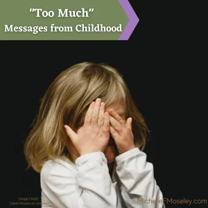 A young child with shoulder length blonde hair and wearing a white, long-sleeved shirt is covering their face with their hands as though ashamed.  