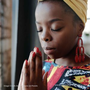 A dark-skinned woman with her eyes closed and her hands folded as if in prayer.