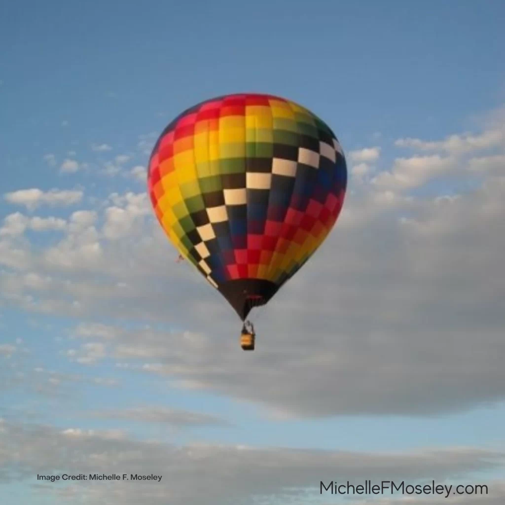 A rainbow colored hot air balloon against a blue sky with white clouds.
