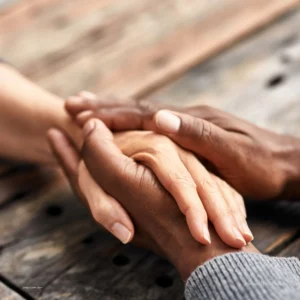 Two brown hands clasp a peach-toned hand to show the connection possible in a trauma-informed and neuro-affirming group.